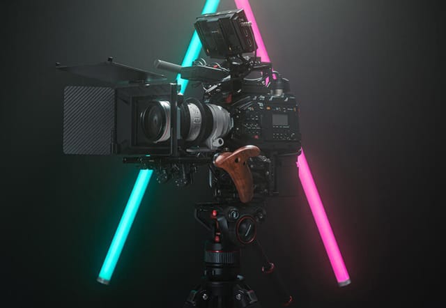 Filmkamera auf Stativ vor grauem Hintergrund mit Neonröhren in Cyan und Pink