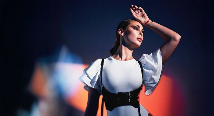 Frau mit erhobenem Arm in Bodysuit im blau-orangen Licht, Fashion-Porträt